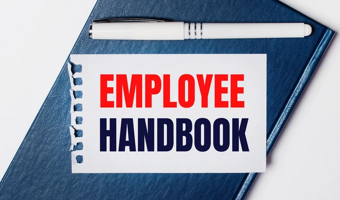 blue diary lies light background has white pen piece paper with text employee handbook 1